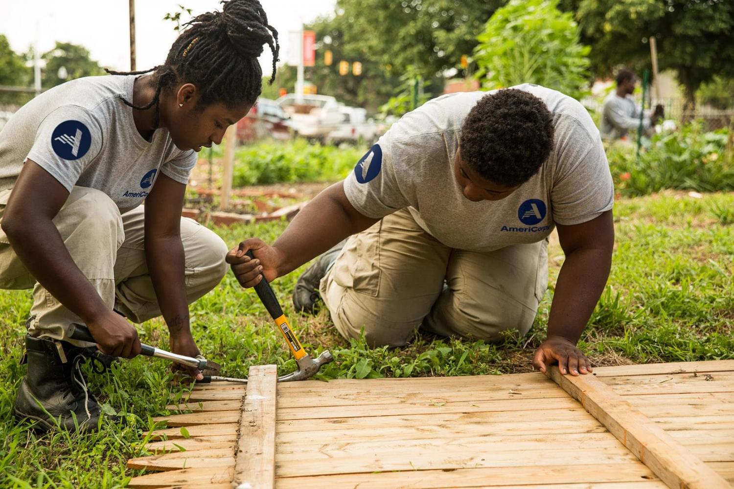 Two women wearing AmeriCorps T-shirts building a fence
