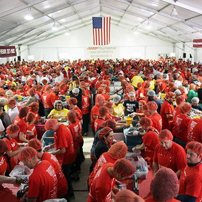 A big group of people in red tops in a large warehouse sorting boxes