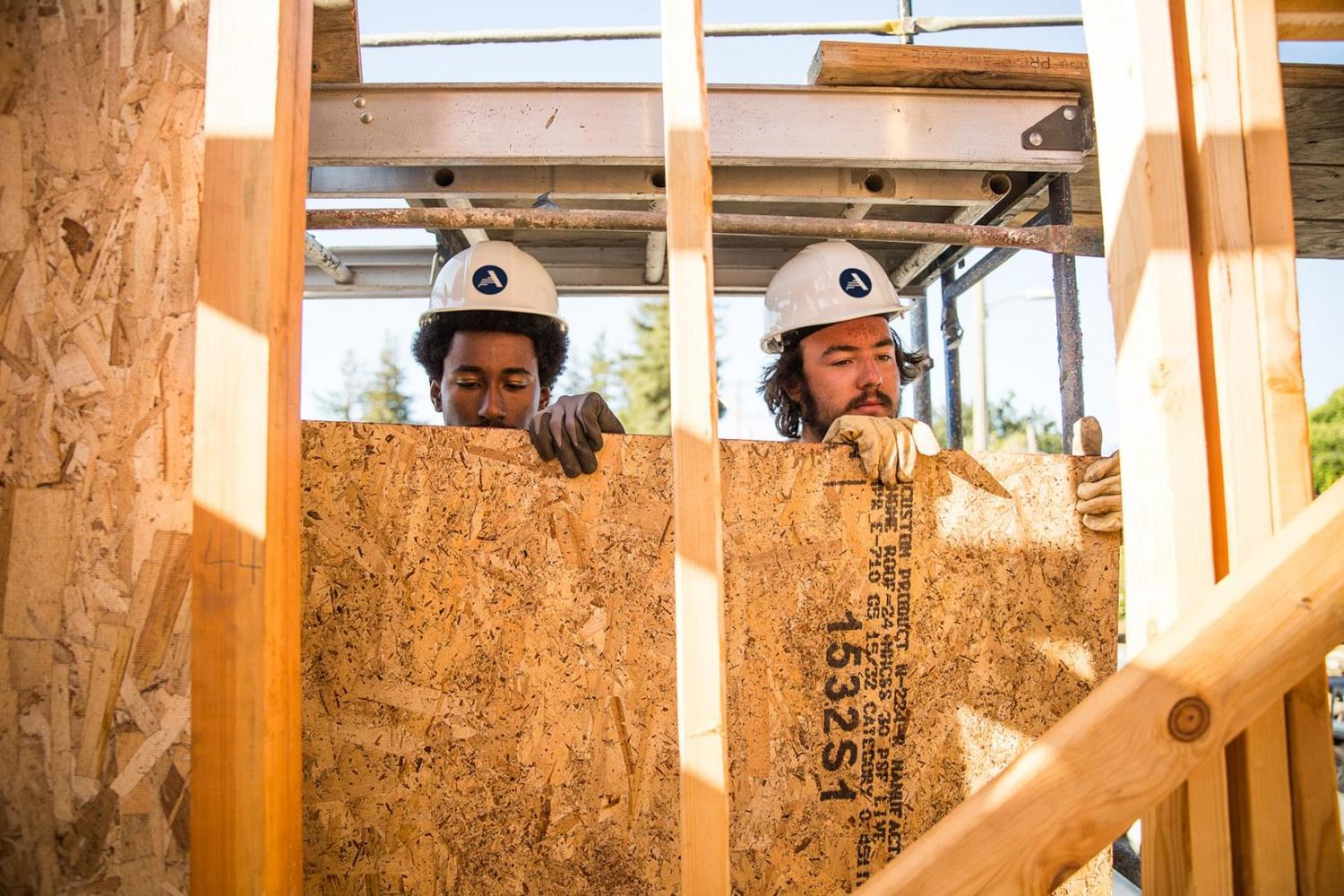 Two men wearing AmeriCorps hard hats building
