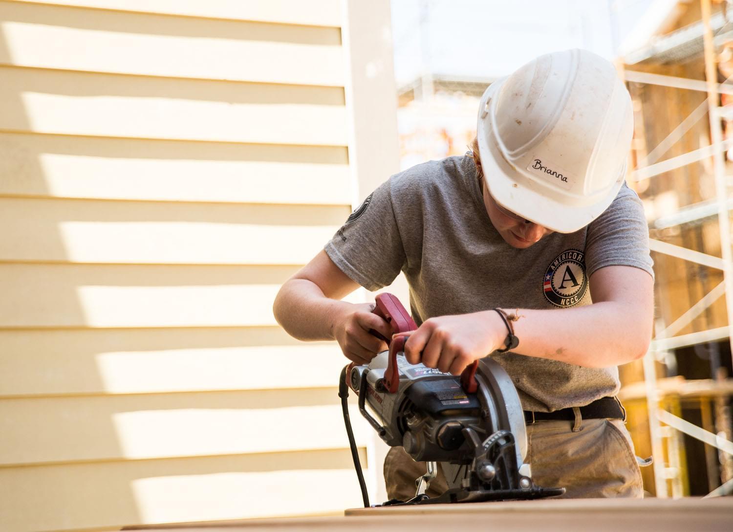 Woman wearing a hard hat using an electric sander