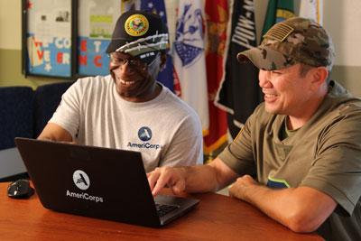 A U.S. military veteran in AmeriCorps discusses a plan with a fellow veteran in front of a laptop computer.