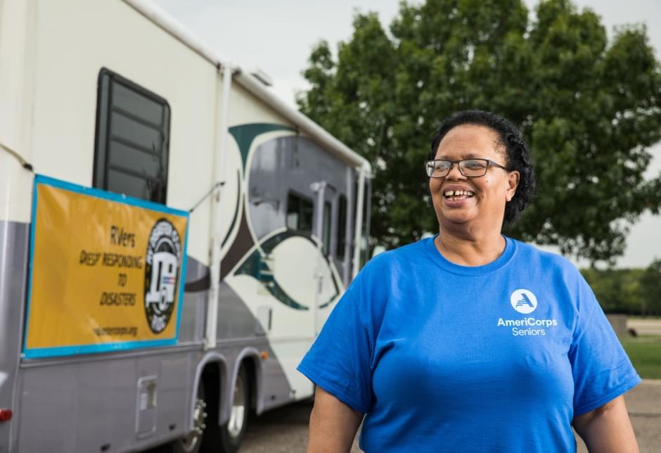 Woman wearing an AmeriCorps Seniors T-shirt standing in front of an RV