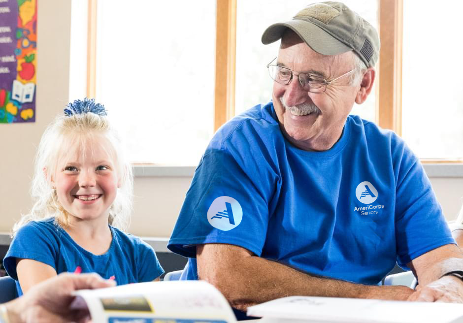 A man wearing an AmeriCorps Seniors T-shirt sitting next to a smiling little girl