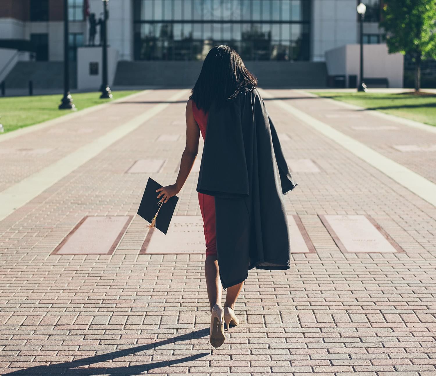 Recent graduate walking on campus with graduation cap and gown