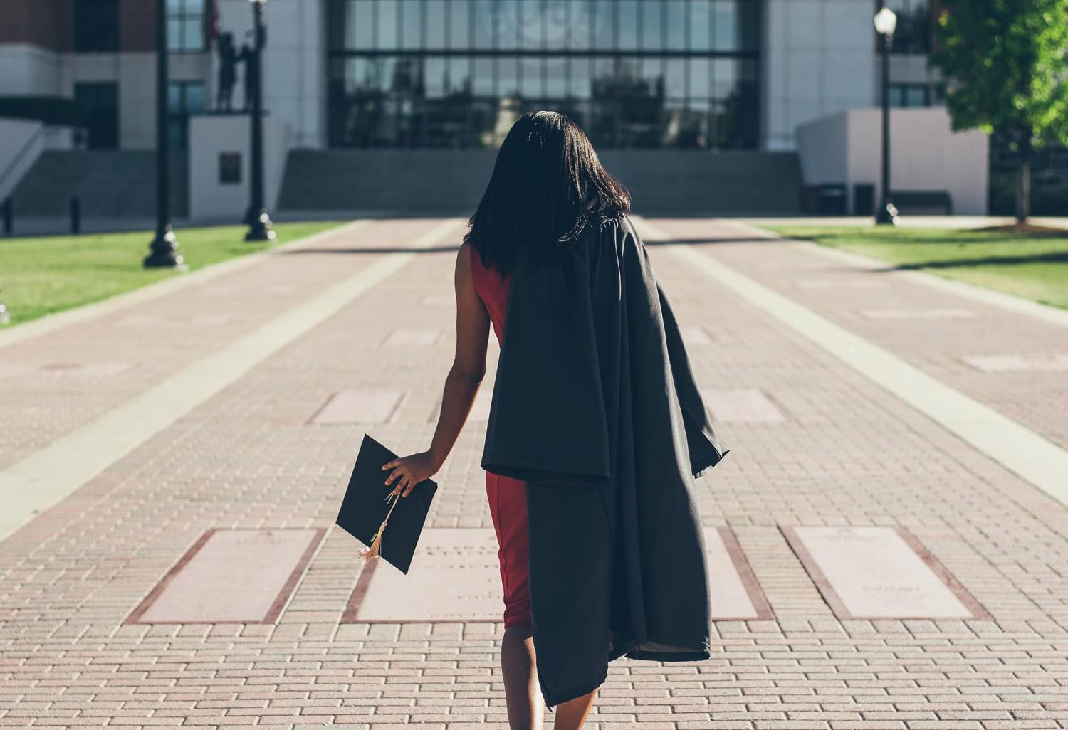 Recent graduate walking on campus with graduation cap and gown