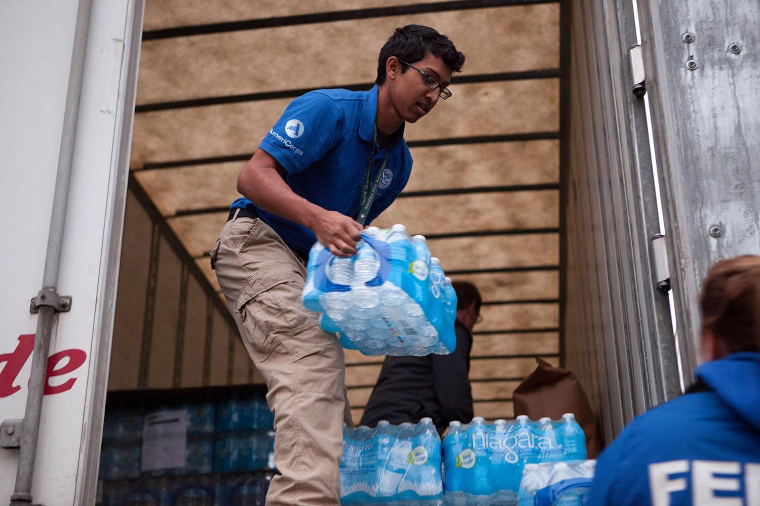Man passing a pack of water bottles out of a truck