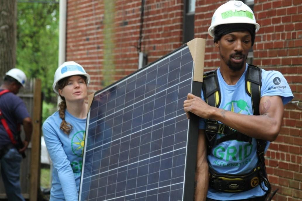 Two AmeriCorps members carry a solar panel