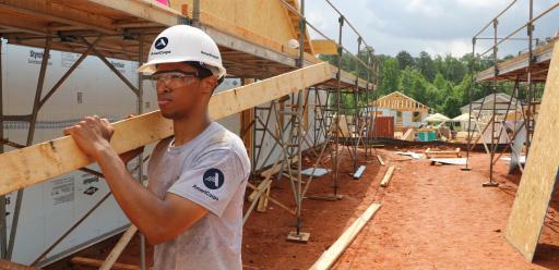 Man wearing an AmeriCorps T-shirt carrying a plank of wood on a building site